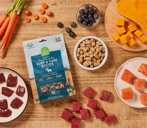 Open Farm pet food package on a wooden table with various pet treats and ingredients.
