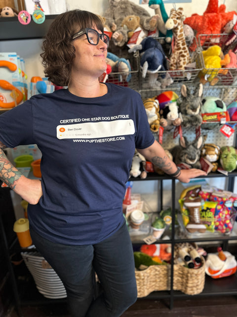 Person wearing a navy blue t-shirt with text standing in front of shelves filled with stuffed animals and toys.
