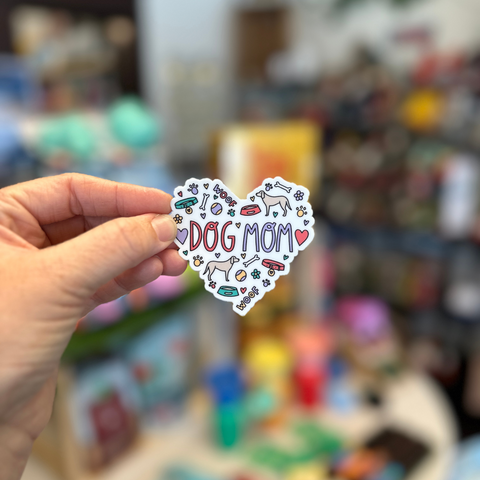 Heart-shaped sticker with 'I love dog mom' text held by a hand against a blurred background