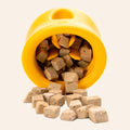 Yellow pet toy with treats spilling out on a white background