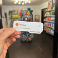A hand holds a white review card in front of a blurred storefront scene. The card shows a profile for Ben Dover with a one-star rating and the handle @PUPTHESTORE.