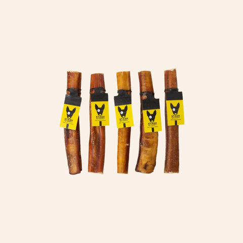 Five dog bully chew sticks with yellow labels on a beige background